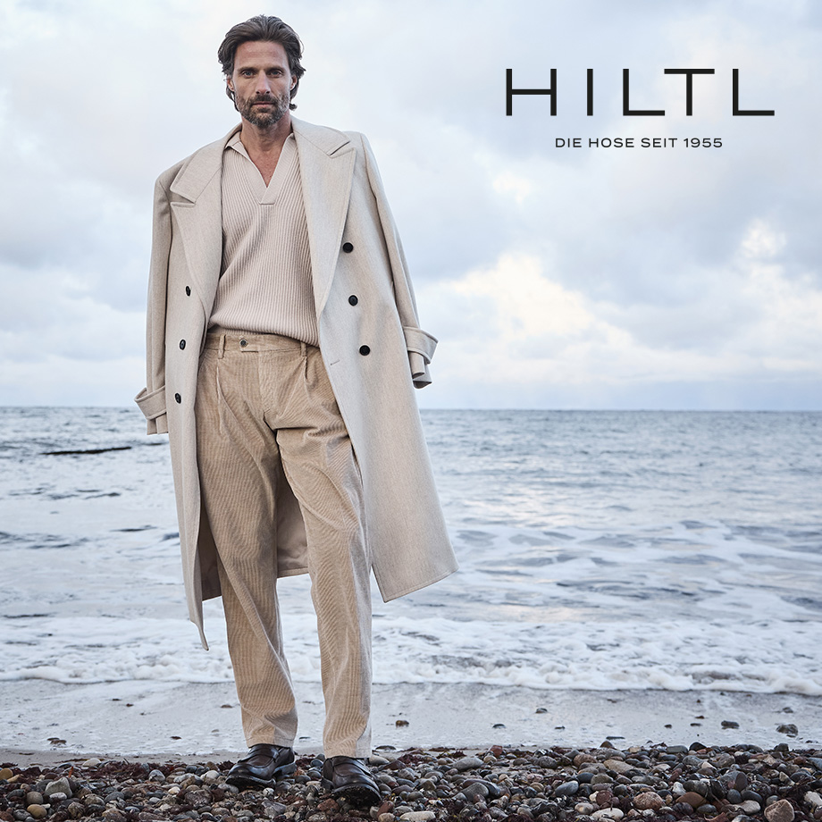 Mann am Strand in beigem Cordanzug mit Mantel, hochwertige Herrenmode