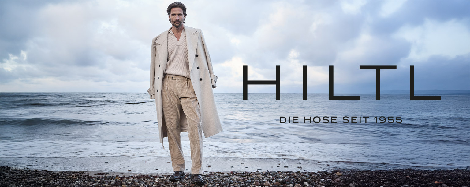 Mann am Strand in beige gestreiften Anzughosen mit passendem Mantel