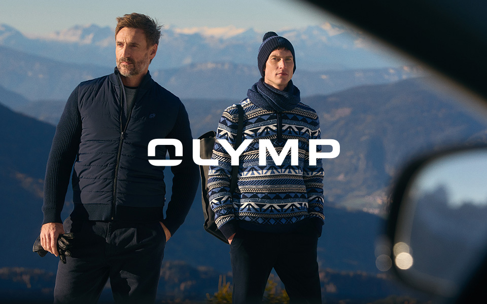 Zwei Männer in Outdoor-Kleidung, einer mit dunkelblauem Steppjacke, der andere mit gemustertem Pullover und Mütze, in Berglandschaft