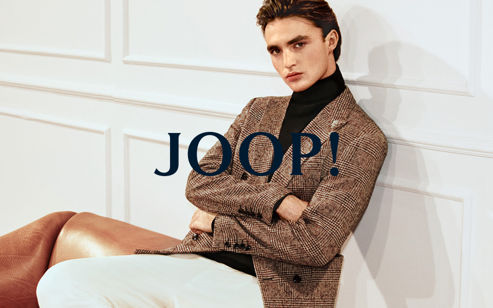 Mann im karierten Sakko mit Rollkragenpullover, elegant sitzend auf einem Sofa