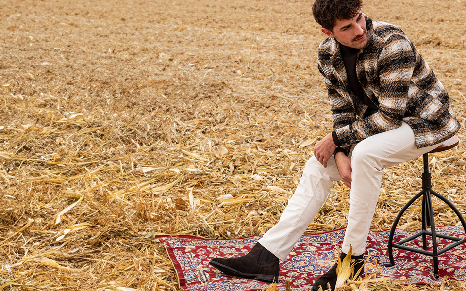 Mann in kariertem Sakko und weißer Hose, draußen auf Hocker sitzend