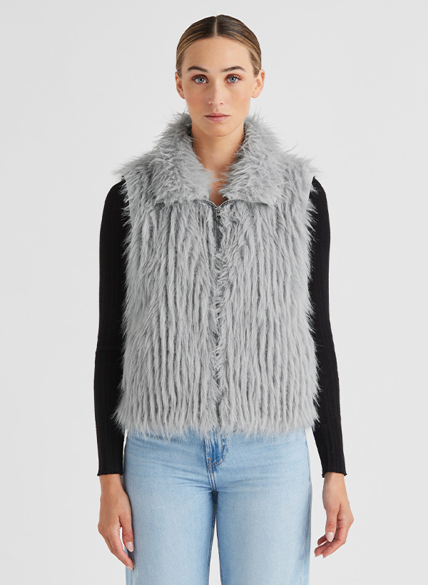 Graue Kunstpelzweste, casual über schwarzem Langarmshirt, hellblaue Jeans.