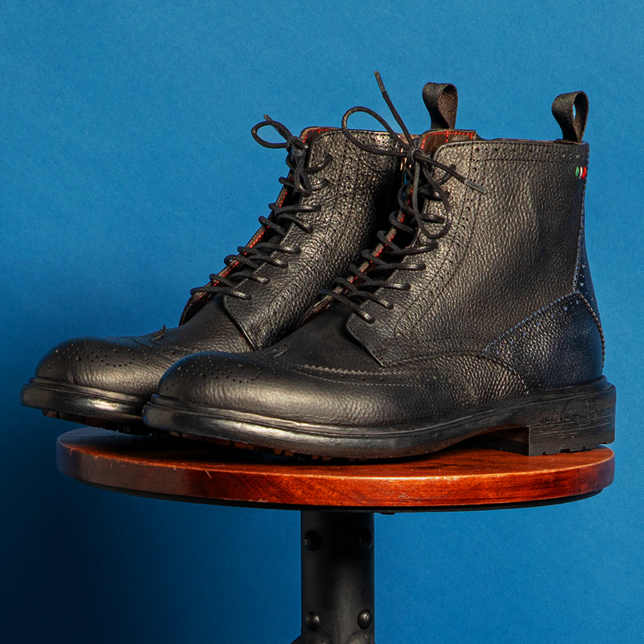 Schwarze Lederstiefel mit feiner Struktur, klassisch geschnürt, auf Holzhocker präsentiert