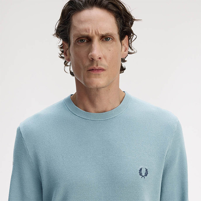 Hellblauer Strickpullover aus Baumwolle, runder Halsausschnitt, getragen von Mann im neutralen Hintergrund