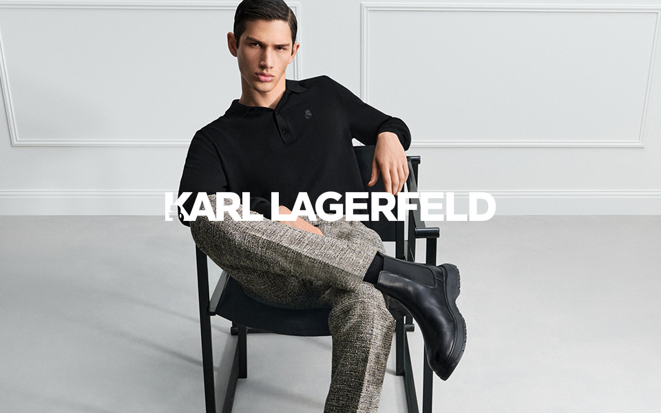 Eleganter Mann in schwarzem Langarmshirt und gemusterter Hose, lässig sitzend mit schwarzen Stiefeln