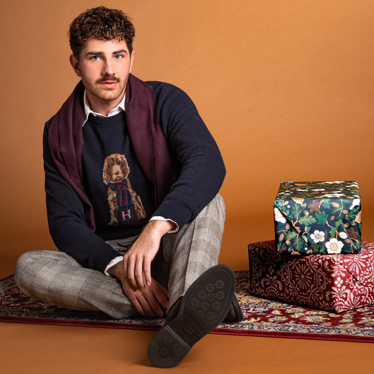 Mann im dunkelblauen Hundemotiv-Pullover und karierter Hose, leger sitzend auf Teppich