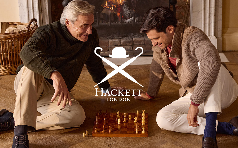 Zwei Männer in Strickpullovern beim Schachspiel vor Kamin, gemütliche Freizeitkleidung