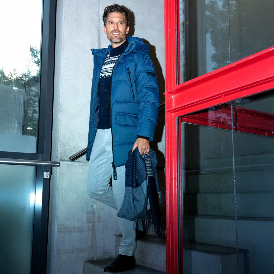 Mann in blauer Daunenjacke mit Norwegerpullover und Schal auf Treppe