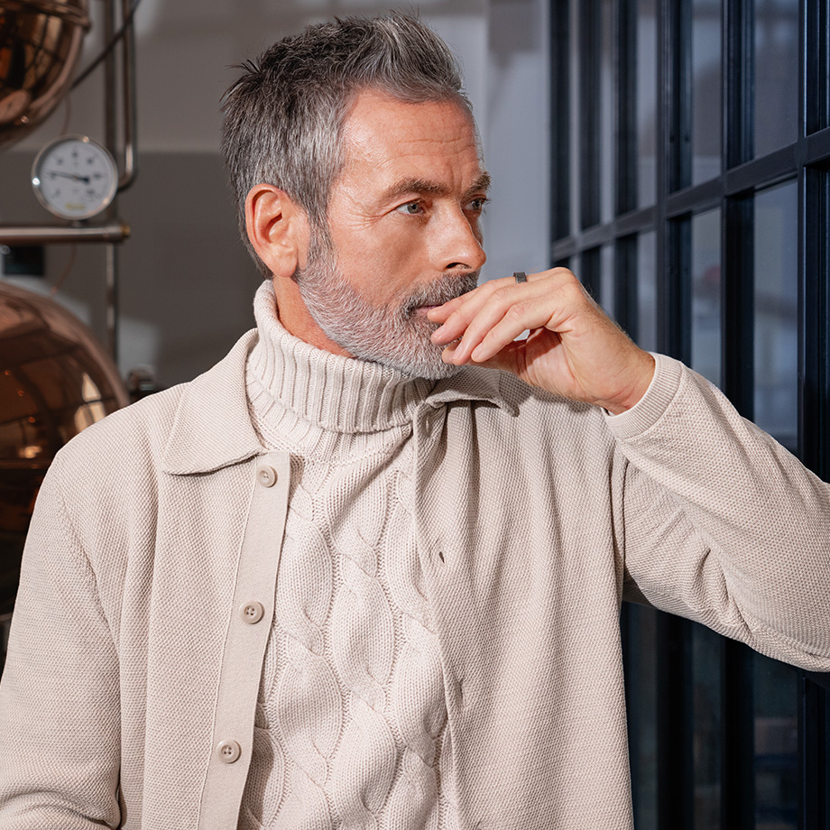 Hellbeiger Strickpullover mit Rollkragen und Zopfmuster, getragen unter sandfarbener Jacke, stilvoll präsentiert