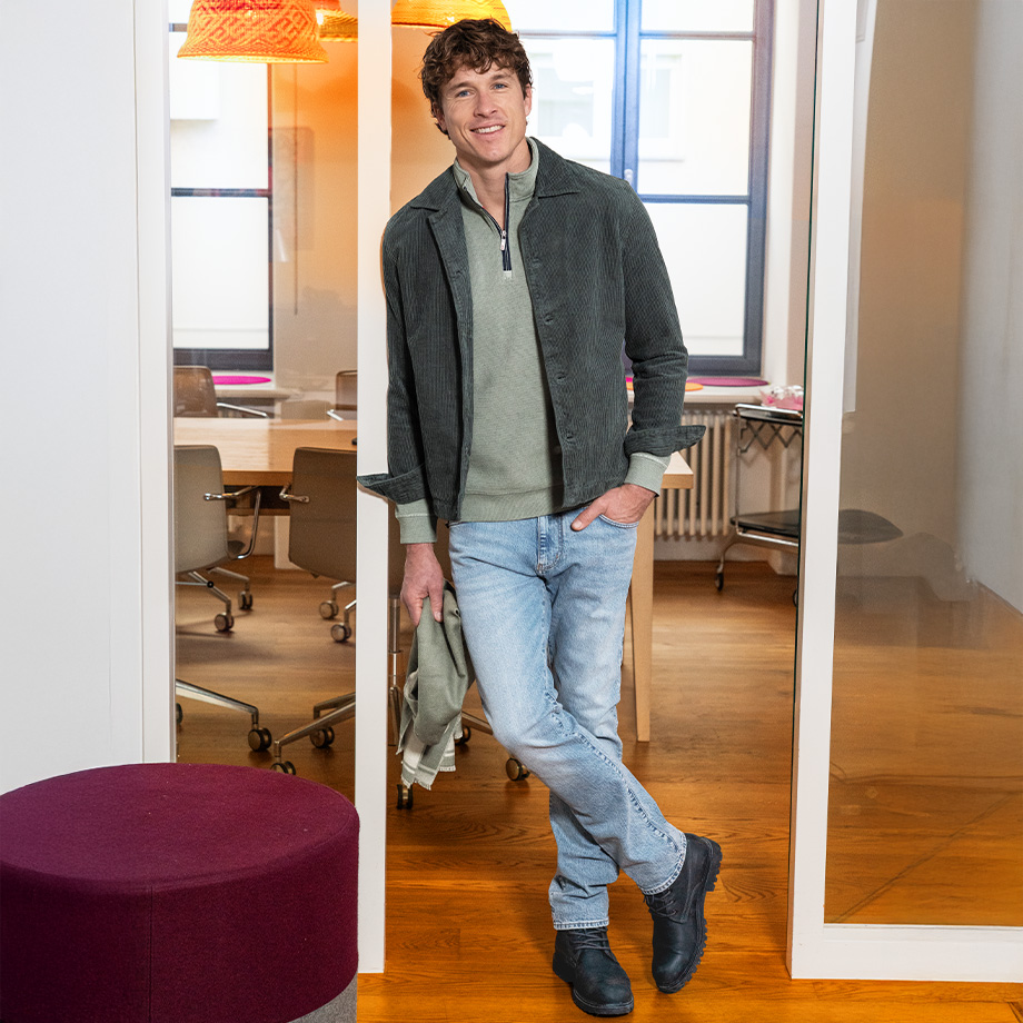 Mann in grauer Cordjacke und hellblauer Jeans im Büro stehend