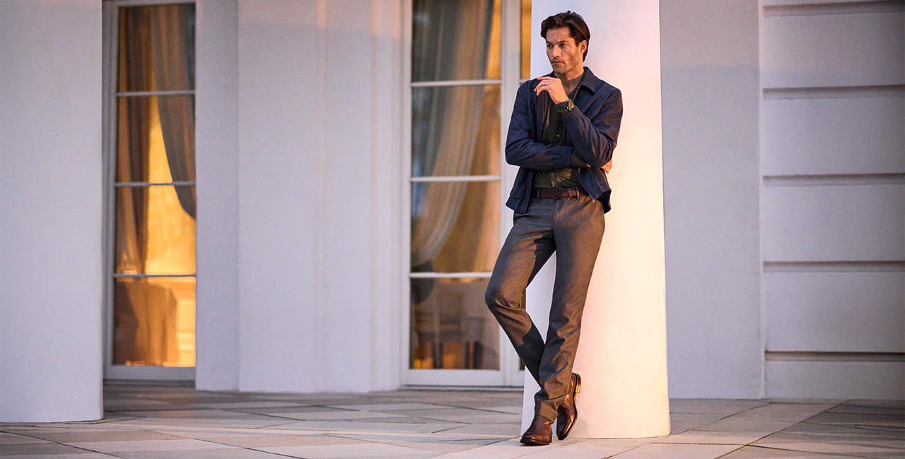 Mann in dunkelblauer Jacke und grauer Hose, leger gegen Wand lehnend