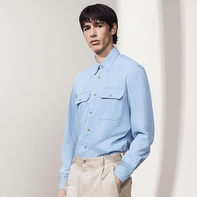 Ein Model trägt ein hellblaues Hemd mit zwei Brusttaschen und eine beige Hose. 