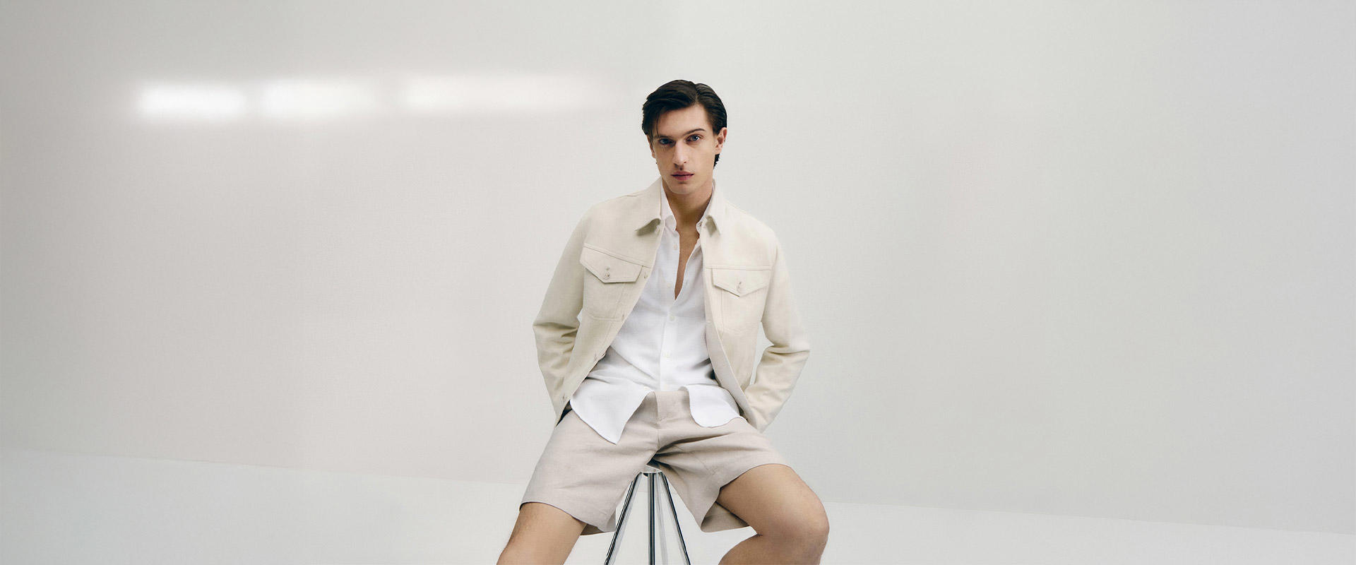 Ein Model trägt ein beiges Overshirt über einem weißen T-Shirt, kombiniert mit einer passenden beigefarbenen Bermuda.