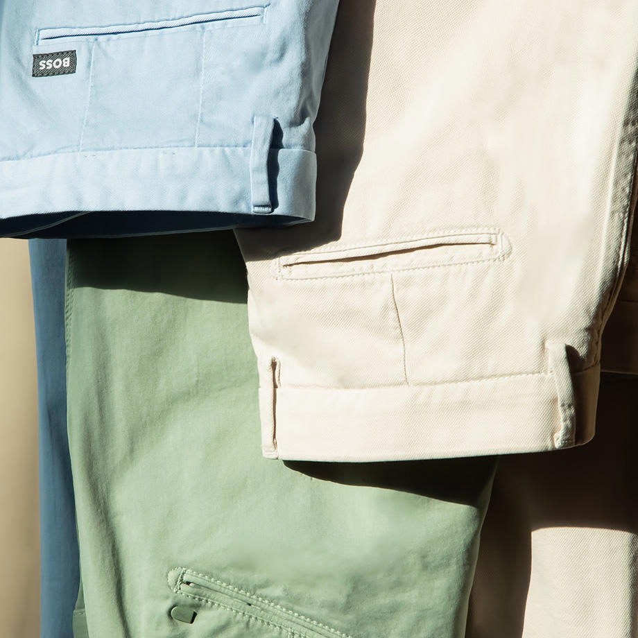 Mehrere Chinohosen in beige, hellbalu und mint hänngen übereinander.