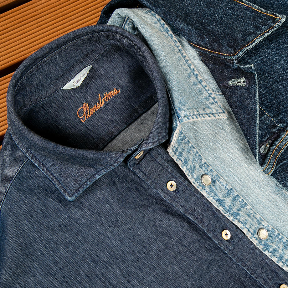 Drei ineinandergelegte Jeanshemden in Hellblau, Mittelblau und Dunkelblau auf einer Holzoberfläche – ein zeitloser Denim-Look mit lässigem Charakter.