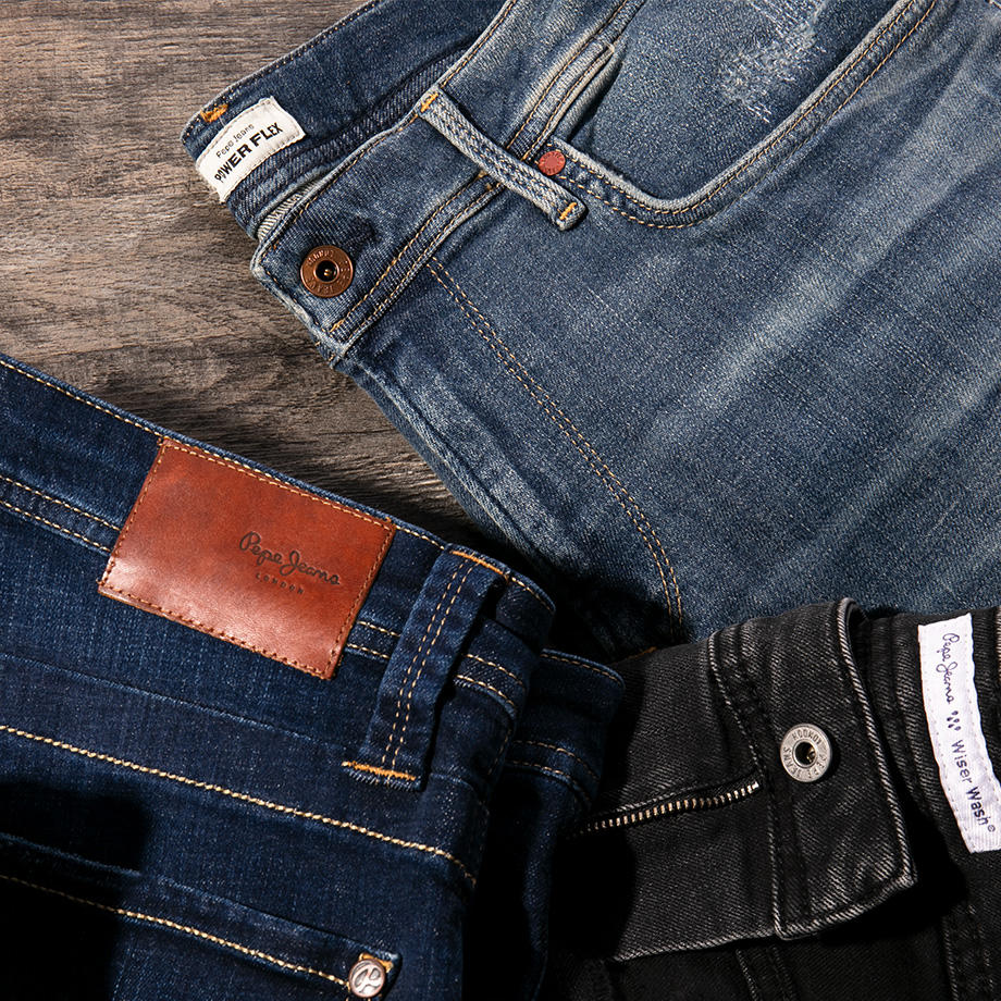 Drei, auf einer Holzplatte übereinandergelegte Jeans, in Schwarz, Mittelblau und Dunkelblau, mit flexiblem Bund für maximalen Tragekomfort und Bewegungsfreiheit.