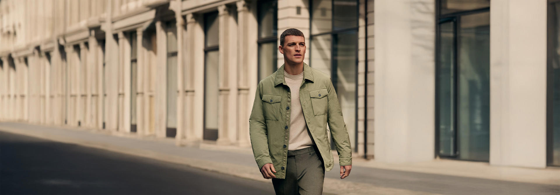 Ein Mann trägt eine olivgrüne Frühlingsjacke und läuft über eine Straße in der Stadt