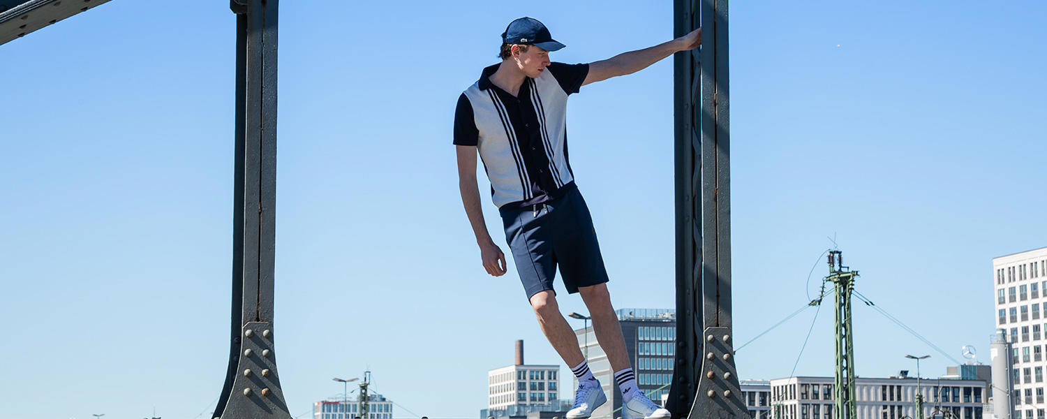 Ein Mann in einem blau-weißen Outfit posiert auf einer Brücke mit der Skyline im Hintergrund