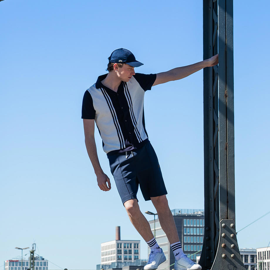 Ein Mann in einem blau-weißen Outfit posiert auf einer Brücke mit der Skyline im Hintergrund