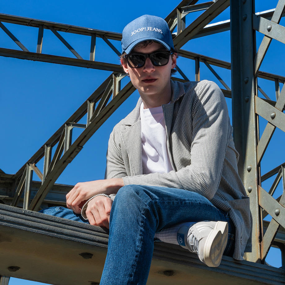 Ein junger Mann trägt ein gestreiftes Sweatsakko. Er sitzt auf einer Brücke.
