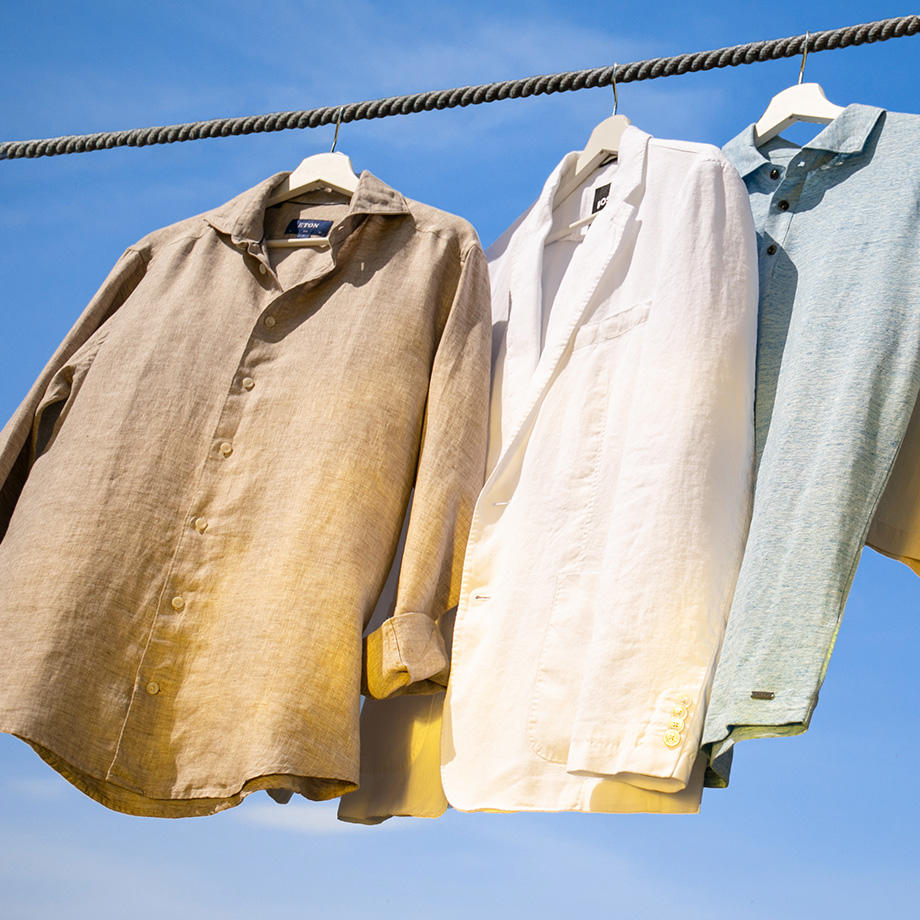 Leichte Sommerhemden aus Leinen hängen vor einem blauen Himmel – Symbolbild für luftige Sommermode.