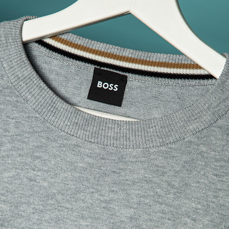 Detailaufnahme eines grauen Pullovers von BOSS auf einem weißen Kleiderbügel.