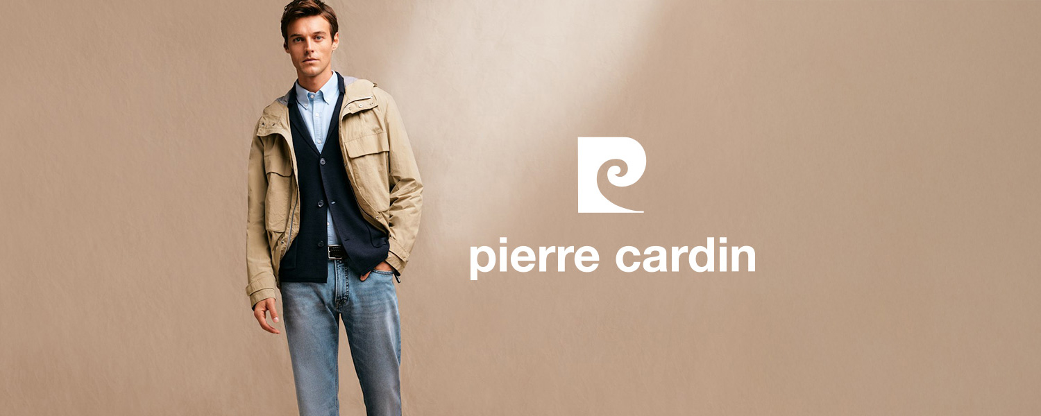 Ein Mann trägt eine beige Jacke über dunkelblauem Cardigan und hellblauem Hemd mit heller Jeans. Er steht vor beigem Hintergrund, oben links ist das Pierre-Cardin-Logo zu sehen