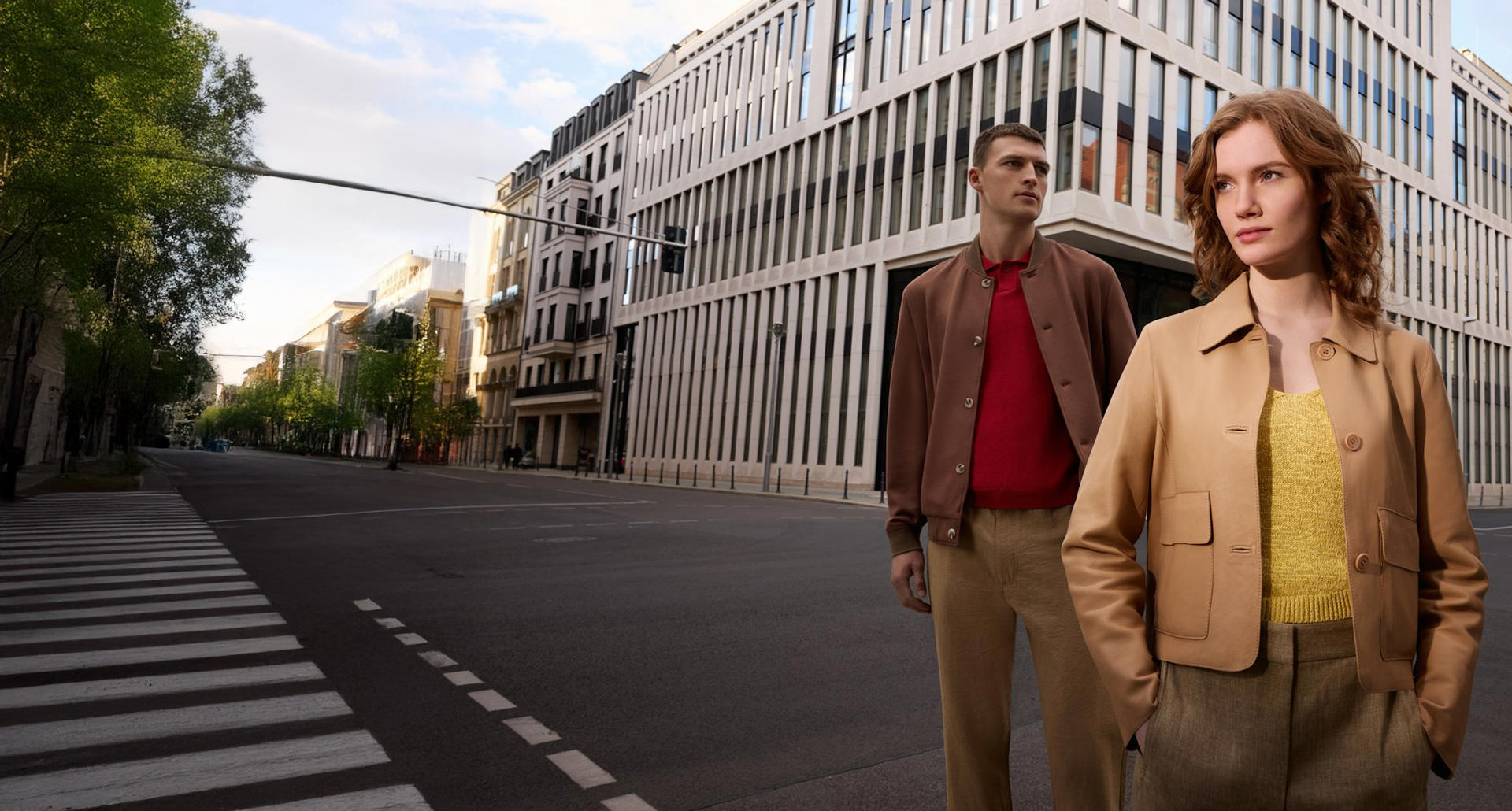 Ein Mann und eine Frau stehen in einer Stadt mit einem Gebäude im Hintergrund. Sie trägt eine beige Lederjacke und er trägt einen dunkelbraunen Blouson