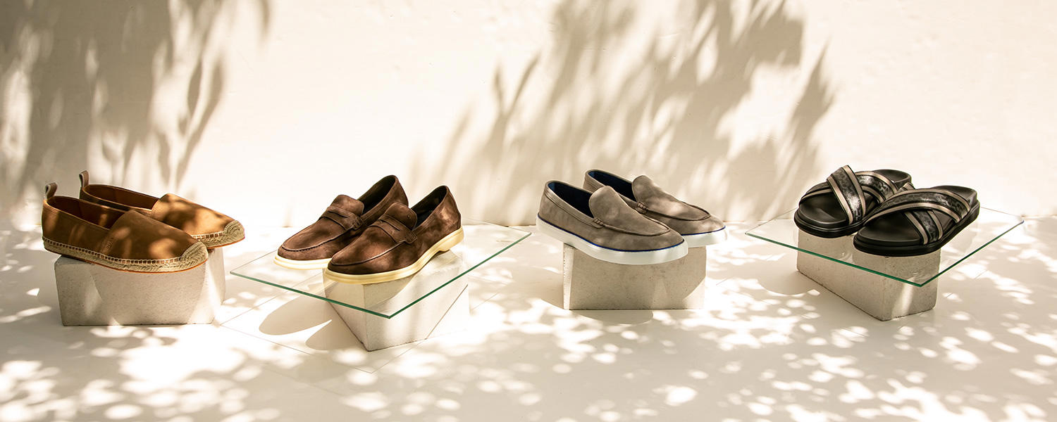 Verschiedene Herrenschuhmodelle – Espadrilles, Loafer, Sneaker und Slipper – dekorativ präsentiert im natürlichen Schattenspiel.