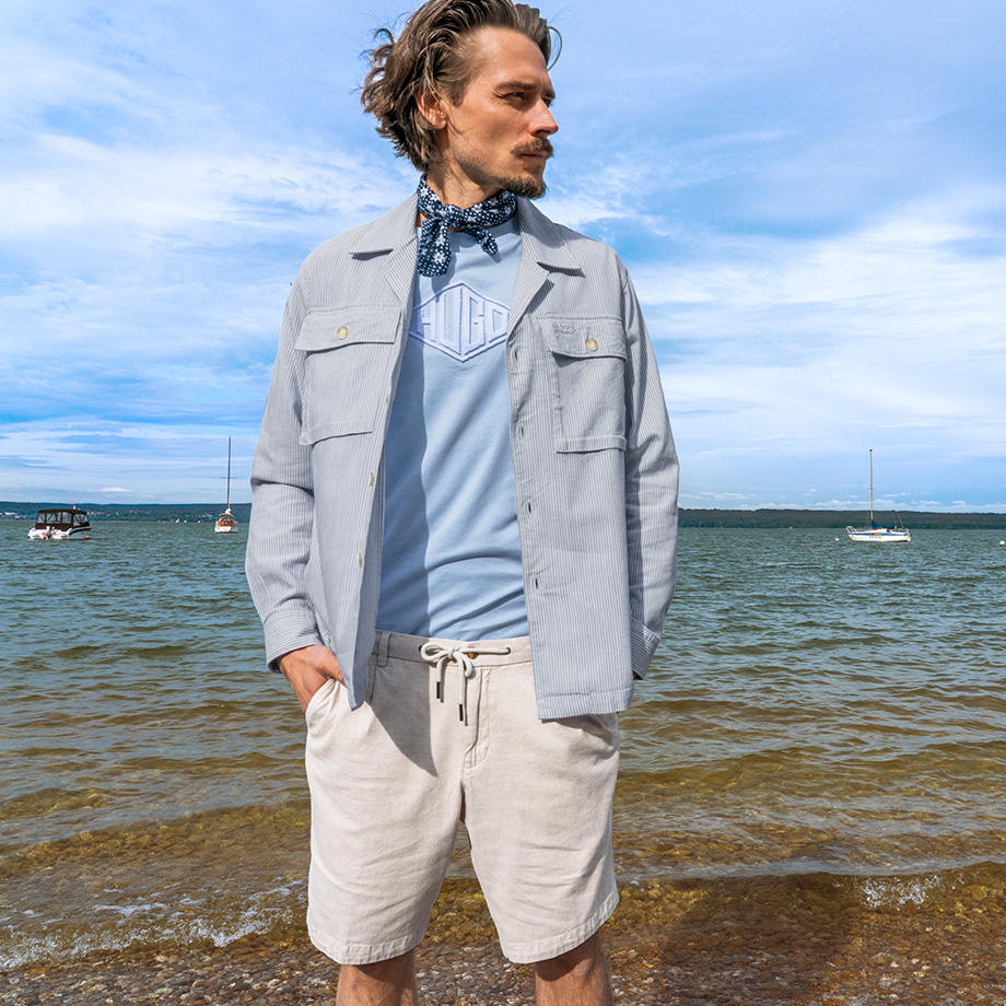 Lässiger Sommerstil am Meer mit hellblauem T-Shirt & Overshirt sowie beiger Shorts.
