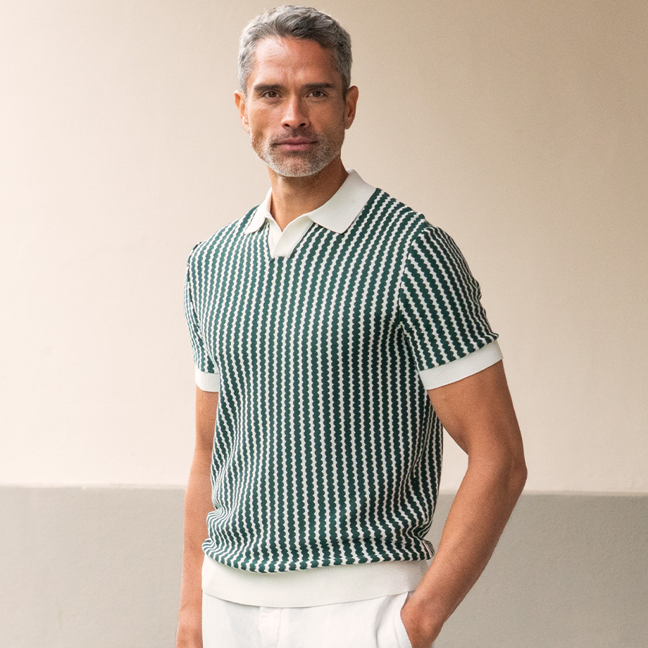 Eleganter Herrenlook mit gestricktem weiß-dunkelgrünem Poloshirt in modernem Design vor neutralem Hintergrund.