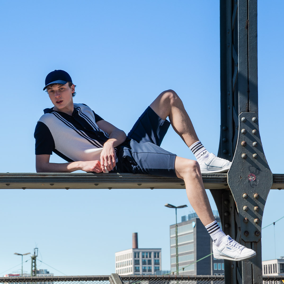 Ein Mann in einem blau-weißen Outfit posiert auf einer Brücke mit der Skyline im Hintergrund