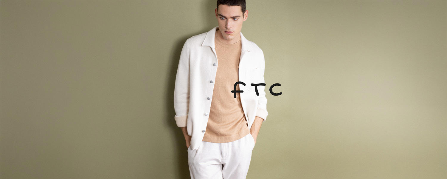 Vor einem khakifarbenen Hintergrund steht ein Mann in einem weißen Overshirt, einem beigen T-Shirt und einer weißen Hose. Im Zentrum des Bildes ist das Logo „FTC“ platziert.
