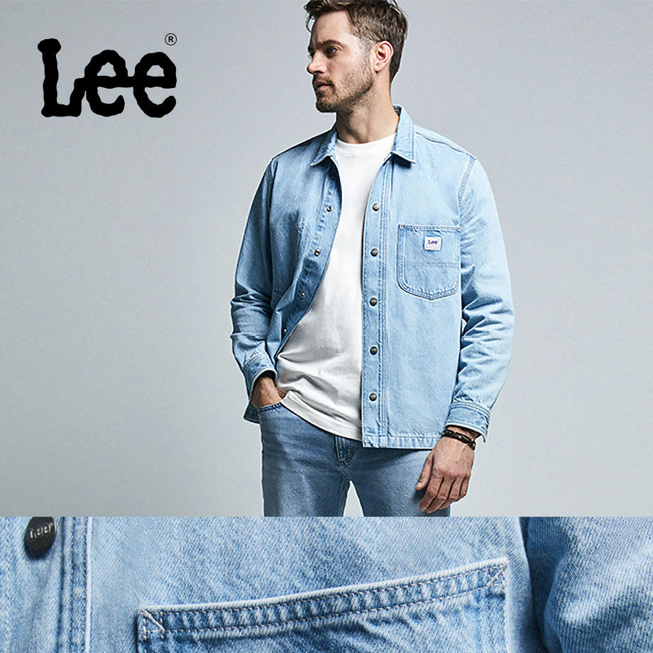 Mann in hellblauer Lee-Jeansjacke und weißem Shirt steht lässig vor grauem Hintergrund.