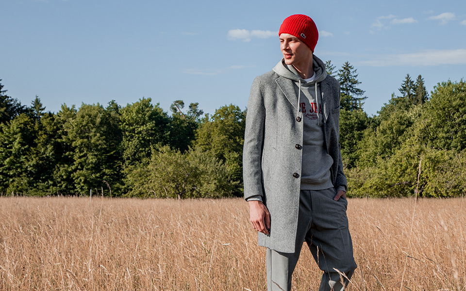 Mann in grauem Mantel und Kapuzenpullover mit roter Mütze im Freien