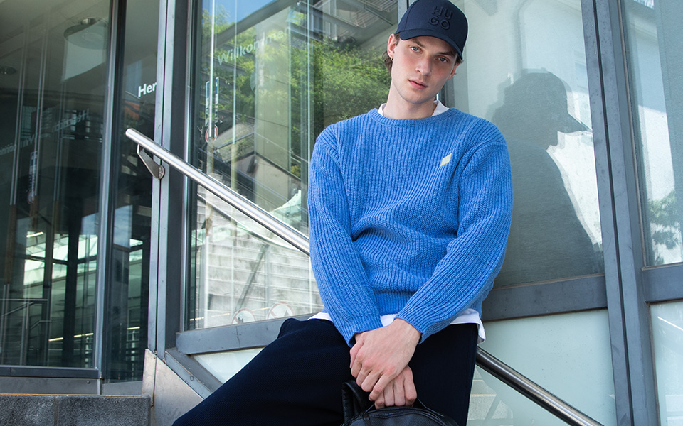 Ein Mann in einem blauen Strickpullover steht auf einer Steintreppe.
