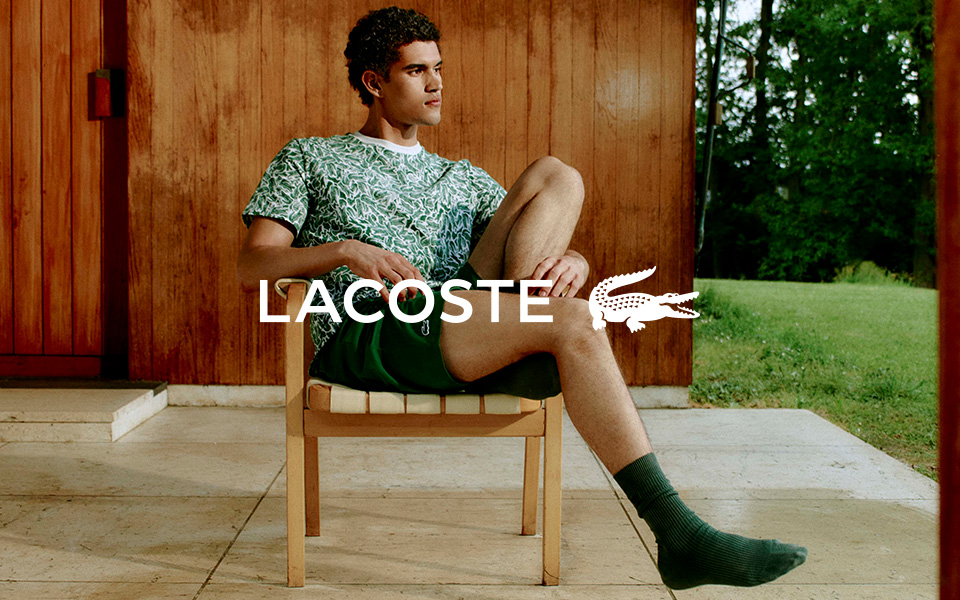 Ein junger Mann in LACOSTE-Kleidung auf einem Stuhl, mittiges LACOSTE-Logo