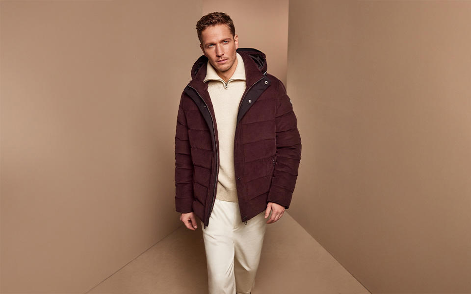 Ein Mann in einer dunkelroten Steppjacke vor neutralem Hintergrund