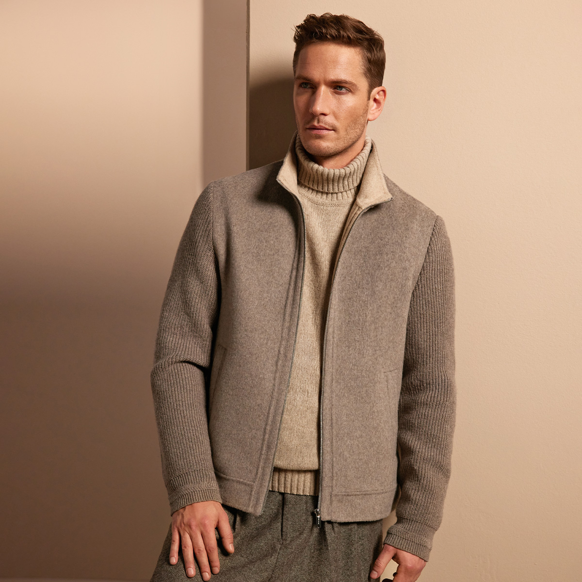 Ein Mann in beiger Wolljacke mit Strickärmeln vor neutralem Hintergrund