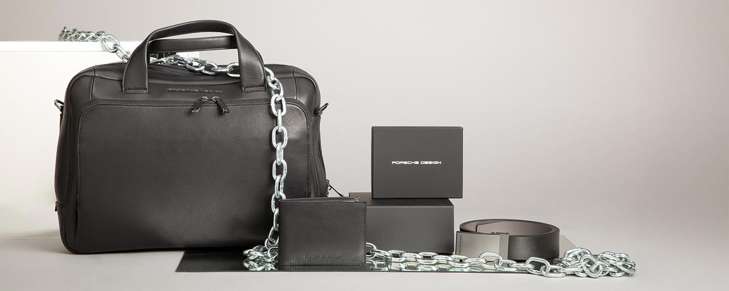 Stylishe schwarze Business-Tasche von Porsche Design mit cooler Chain-Detail, Uhr und Parfum – perfekt für einen cleanen, urbanen Look.
