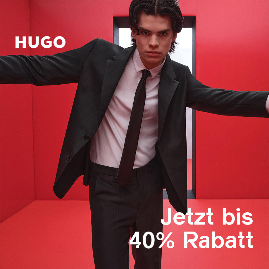 Ein Mann in schwarzem Anzug, weißen Hemd und schwarzer Krawatte von HUGO steht mit ausgestreckten Armen vor rotem Hintergrund. Aufschrift: 'Jetzt bis 40 % Rabatt'.