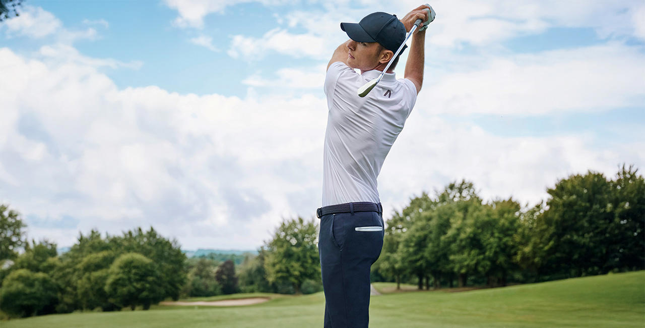 Mann in sportlichem Golf-Outfit mit Cap schwingt den Schläger auf grünem Fairway – Herren Golfmode für Performance und Stil.