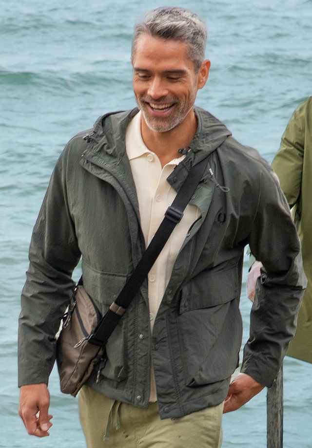 Alt Text: Zwei Männer in leichten Outdoor-Jacken spazieren entspannt an einem Steg am Wasser.