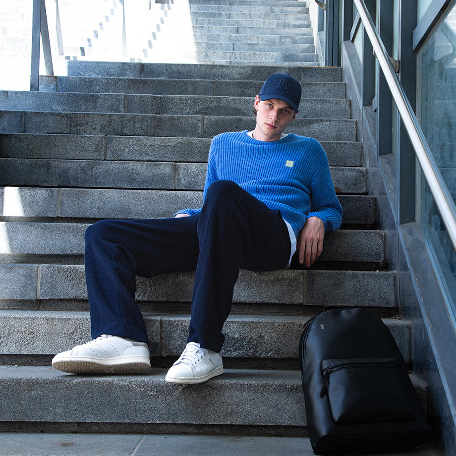 Ein Mann in einem blauen Strickpullover sitzt auf einer Steintreppe.