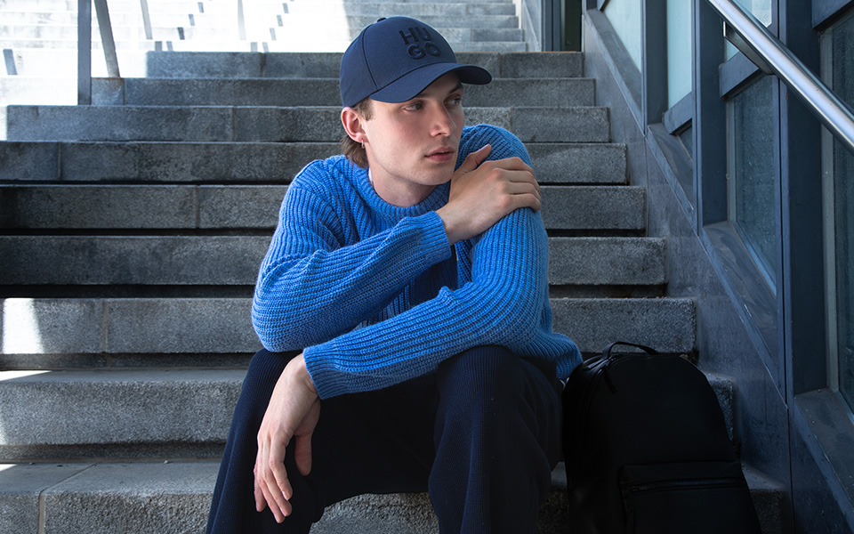 Ein junger Mann sitzt auf einer Steintreppe und trägt einen blauen Grobstrickpullover.