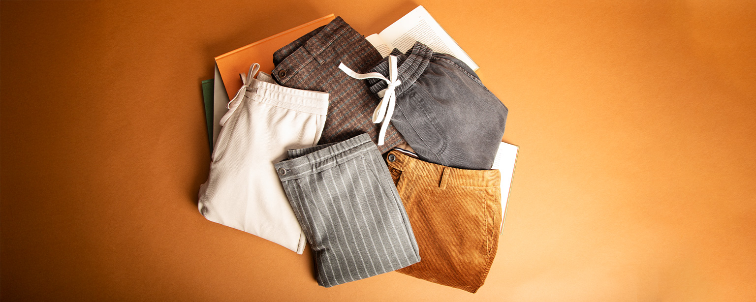 Gefaltete Herrenbekleidung bestehend aus Cordhose, Stoffhose und Jogpant in Naturtönen – modische Herbst- und Wintermode für Männer.