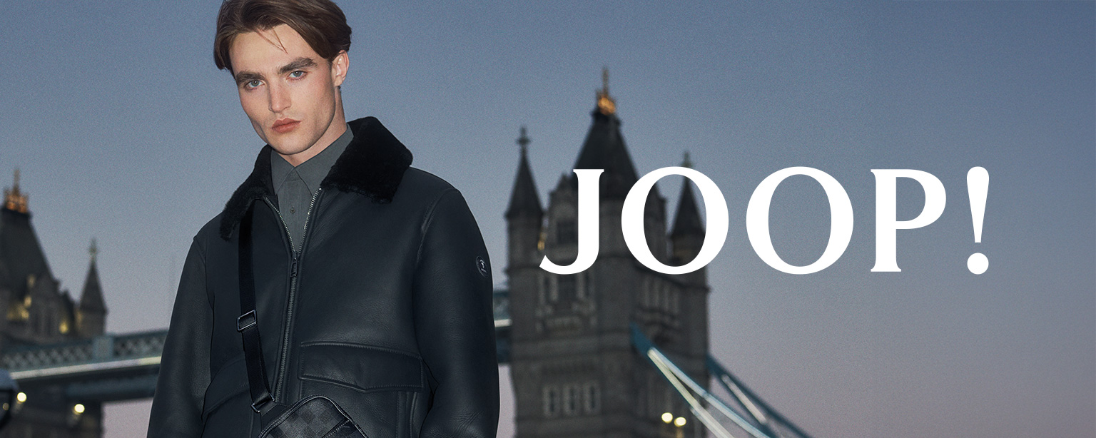 Stilvoller Mann in schwarzer Lederjacke mit Umhängetasche von JOOP! vor urbaner Kulisse – luxuriöse Herrenmode mit Statement bei Herrenausstatter.de.