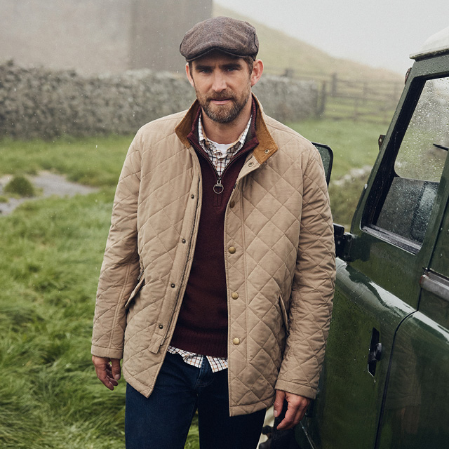 Ein Mann in einer beigen Steppjacke von Barbour auf dem Feld
