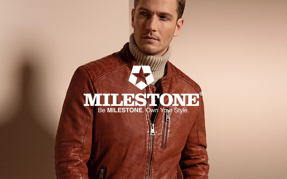 Ein Mann in einer rostfarbenen Lederjacke vor beigem Hintergrund. Mittiges Logo von Milestone