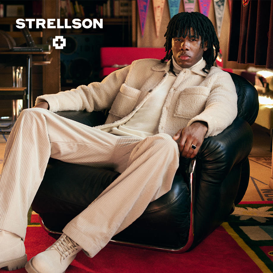 Ein Mann im cremefarbenen Fleece-Set sitzt entspannt in einem modernen Sessel; Strellson präsentiert einen urbanen, lässigen Winterlook.